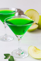 close-up Apple cocktail mixed drink with vodka and apple slice. Apple martini cocktail on the white table. Green Alcoholic drinks in martini glasses with apple slice and shaker. copy space.