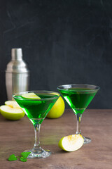 Apple cocktail mixed drink with vodka and apple slice. Apple martini cocktail on the black background. Green Alcoholic drinks in martini glasses with apple slice. copy space.