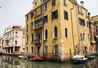 Fototapeta na wymiar Venetian street, Venice waterway, classical buildings, Venetian architecture, moored boats, shutters, flowers in windows, Italy