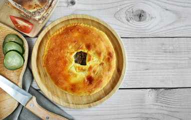 The traditional dish of the peoples of the Caucasus is Karachai khychins (Ossetian pies) with meat on a wooden board. Light wooden background, top view, copy space.
