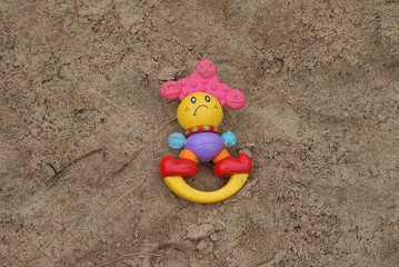 Fototapeta na wymiar one colored plastic toy rattle lies in the gray sand of the sandbox on the street