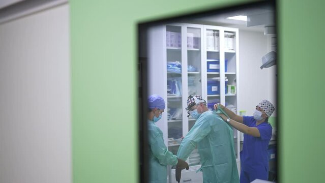 Chief surgeon being prepared for surgery. Process of dressing of a doctor in special uniform peeped through a window in surgery room door.