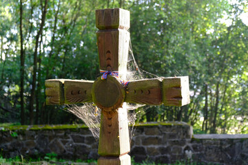 Old wooden cross with spider's web lit by sun in First World War cemetery in the village of Krempna in morning light. Low Beskids Mountains, Poland