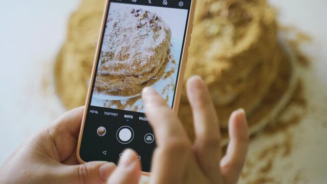 Female hands take photos of homemade cake in the kitchen on a smartphone. A blogger takes pictures, a photo review of food on a mobile phone camera. Photographing food. Home kitchen.