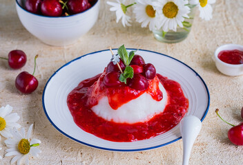 Dessert, thick jelly or pudding with cherry sauce on a white plate on a light concrete background. Dessert recipes without baking.