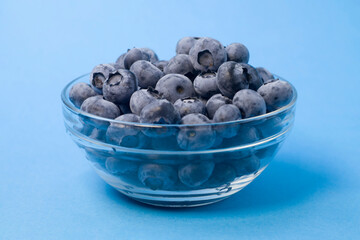 Organic blueberries in glass bowl on blue background, front view. Concept of vegan, freshness, natural food