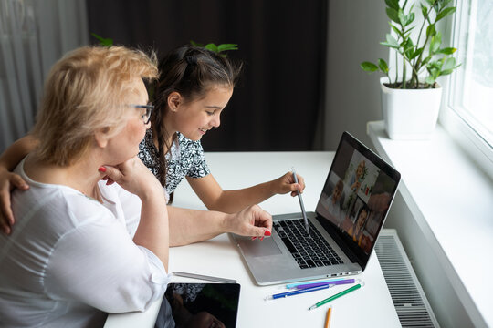 Portrait Of Happy Grandmother And Little Granddaughter Making Video Conference On Pc Sitting At Table, Waving Hands At Screen, Greeting Somebody, Chatting With Parents, Enjoying Online Communication.