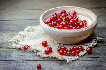 Red currants in a bowl on a canvas napkin on a wooden table.