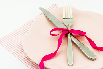 Cutlery with red ribbon on a plate on the table.