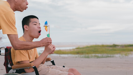 Young man with disability and father blow the windmill by blowing strong air from its mouth. It is...