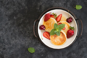 Cottage cheesecakes with berries and mint in a white plate on a dark background.