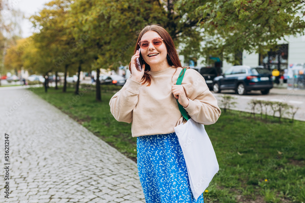 Wall mural beautiful stylish woman in trendy wear spending time on street using smartphone. happy redhead girl 