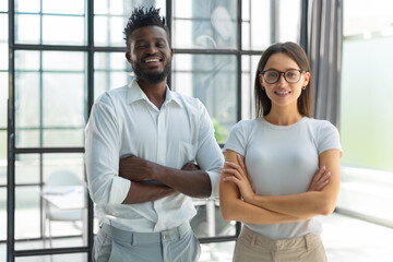 African woman and caucasian man looking at camera standing in office. Multicultural company...