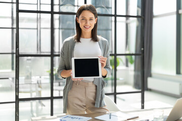 Young happy business woman showing blank tablet computer screen in office