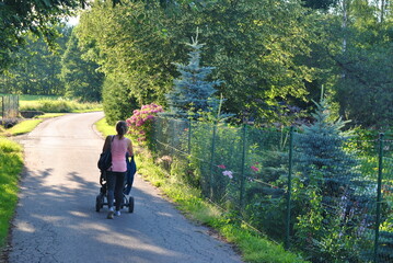 zdjęcie przedstawiające młodą kobietę idącą na spacer z wózkiem wśród ogrodów