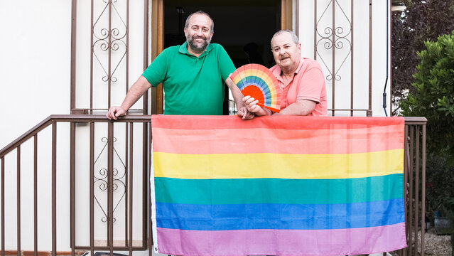 Positive gay couple on balcony with LGBT flag