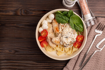 On a wooden table, a plate with pasto1 fettuccine with chicken in creamy mushroom sauce, top view, flat lay, open space