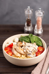 On a wooden table, a plate with pasto1 fettuccine with chicken in creamy mushroom sauc