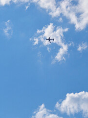 The passenger airplane is flying far away in the blue sky and white clouds. Aircraft in the air. Light vertical background or illustration about international passenger air transportation