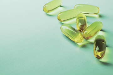 Fish oil. Yellow softgels lie on a green surface. Vitamins and a healthy lifestyle. Background or backdrop. Copy-space for text. Softgel closeup. Omega-3 fatty acids. Macro