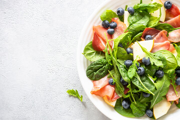 Healthy green salad with jamon, pear and blueberry. Top view on white background, close up.