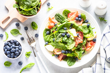 Healthy salad with spinach, jamon, pear and blueberry. Top view on white background.