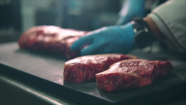 Unknown male chef hands in gloves holds knife cutting raw beef steak into pieces at restaurant kitchen, close up shot. Food, professional occupation, cooking concept