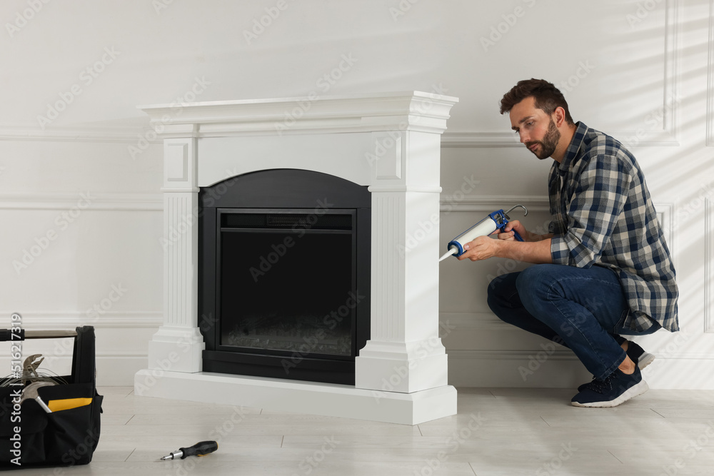 Poster Man sealing electric fireplace with caulk near white wall in room