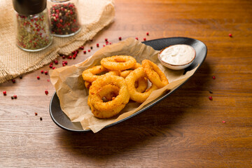 Onion rings in batter with sauce on wooden table