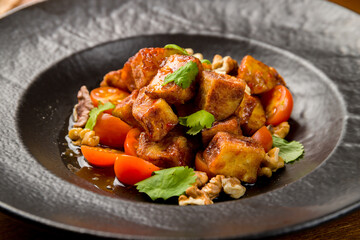fried eggplant in sweet sour sauce with tomatoes and cilantro on black plate