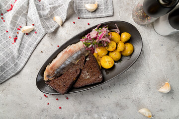 Herring with potatoes and red onion on black plate