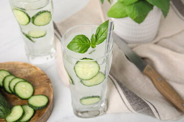 Tasty fresh cucumber water with basil on white table
