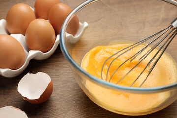 Fototapeta na wymiar Whisking eggs in glass bowl on wooden table, closeup
