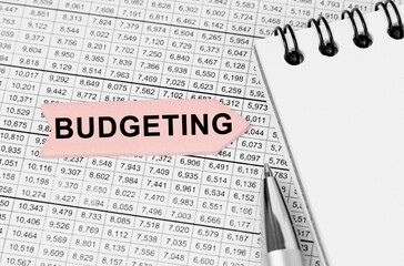 Fototapeta premium On the table among the reports is a notebook, a pen with an arrow with the inscription - BUDGETING