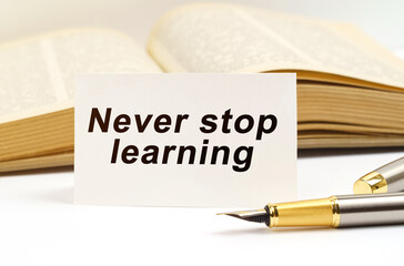 Against the background of the book lies a pen and a business card with the inscription - Never stop learning