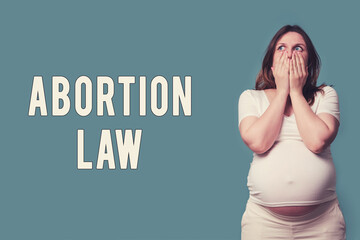 The inscription abortion law and shocked pregnant woman, studio shot on blue background