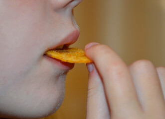 A young girl eats potato chips, a close-up of a woman's mouth bites the chips, copy space....