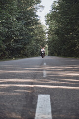 A young happy couple rides a motorcycle on an asphalt road in the forest, freedom and speed