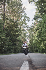 A young happy couple rides a motorcycle on an asphalt road in the forest, freedom and speed