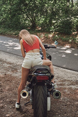 Fototapeta na wymiar Young woman biker drives a motorcycle on a forest road, travels alone