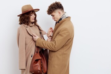 a man helps a woman to fasten her stylish brown coat, standing on a white background and looking at her with love