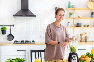 Healthy lifestyle, diet, weight loss concept. Beautiful happy woman cooking healthy food, breakfast from fresh green smoothie standing in his home kitchen looking at the camera and smiling friendly