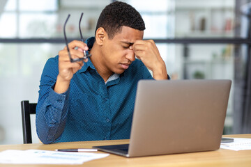 Portrait of tired stressed African American man having headache feeling sick, tired sitting at the...