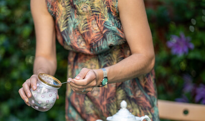 woman in summer dress sweetens from sugar bowl, sugar in garden - obrazy, fototapety, plakaty