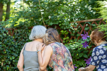 daughter hugs mother, great grandmother on side, womens in garden, family generation