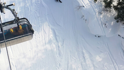 Aerial top view of a moving funicular with people sitting in it on snowy slope background. Footage. Cable car in snowy forest, sport and vacation concept.