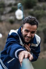 A young man smiling while leaning out from a pedestrian bridge in nature