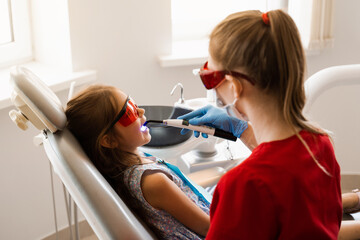 Child dentist treats and removes caries in a patient. Uv illumination of photopolymer tooth filling procedure. Child dentistry.