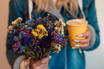 A girl holds flowers and a paper cup with coffee in her hands