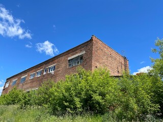 Fototapeta na wymiar Old brick industrial building in sunny weather. Building exterior of shabby unkempt building in countryside on background of blue sky with white clouds.